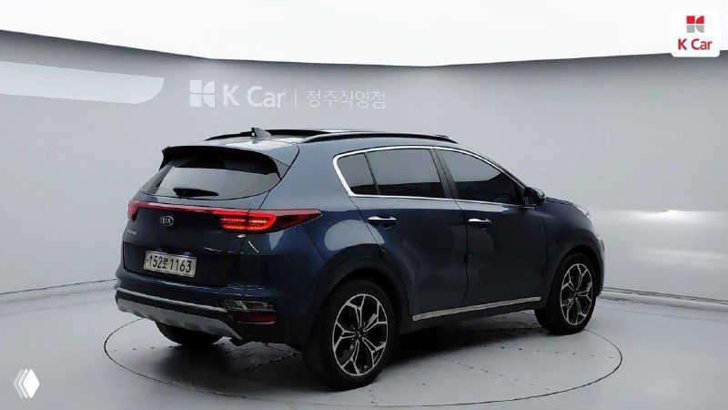 Вид сзади и боковой профиль KIA Sportage 2021 в освещённом павильоне, видны задние фонари, форма багажной части и общий лакокрасочный фон.