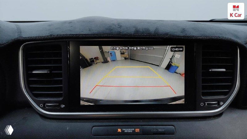 Экран мультимедийной системы KIA Sportage с изображением камеры заднего вида и парковочной разметкой, видно интерфейс и окружение торпедо.