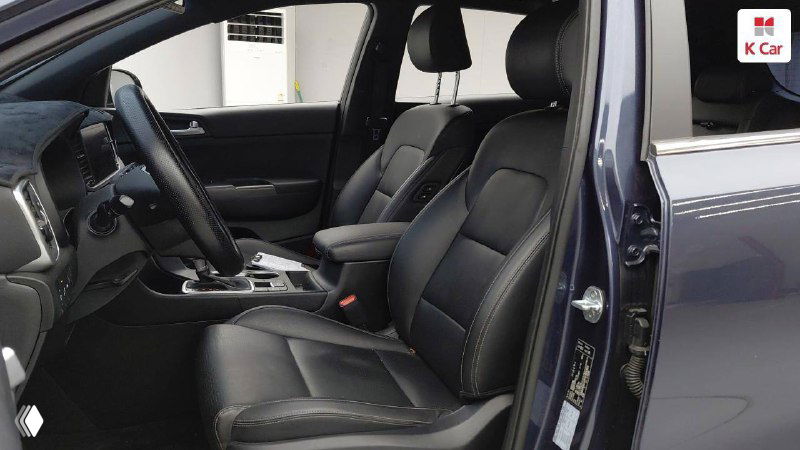 Передние кресла KIA Sportage Prestige 2021 в тёмной кожаной отделке, вид на состояние обивки, подлокотник и пространство в передней части салона.