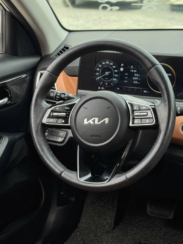 Рулевое колесо и панель приборов KIA Seltos — крупный план руля с логотипом KIA и цифровой приборной доской на фоне салона.