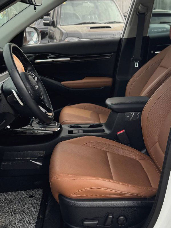 Передние сиденья в коричневой кожаной отделке KIA Seltos — вид боковой посадки, подлокотник и часть приборной панели.