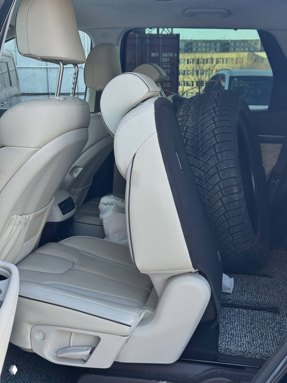 Задний ряд салона Hyundai Palisade с откинутым сиденьем и запасным зимним колесом в багажном отсеке; вид деталей крепления и покрытия пола.