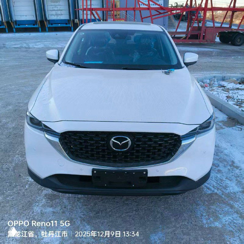 Фронтальный кадр белой Mazda CX-5 на стоянке порта, без номеров, заметен снежный фон и промышленное окружение склада в Уссурийске.