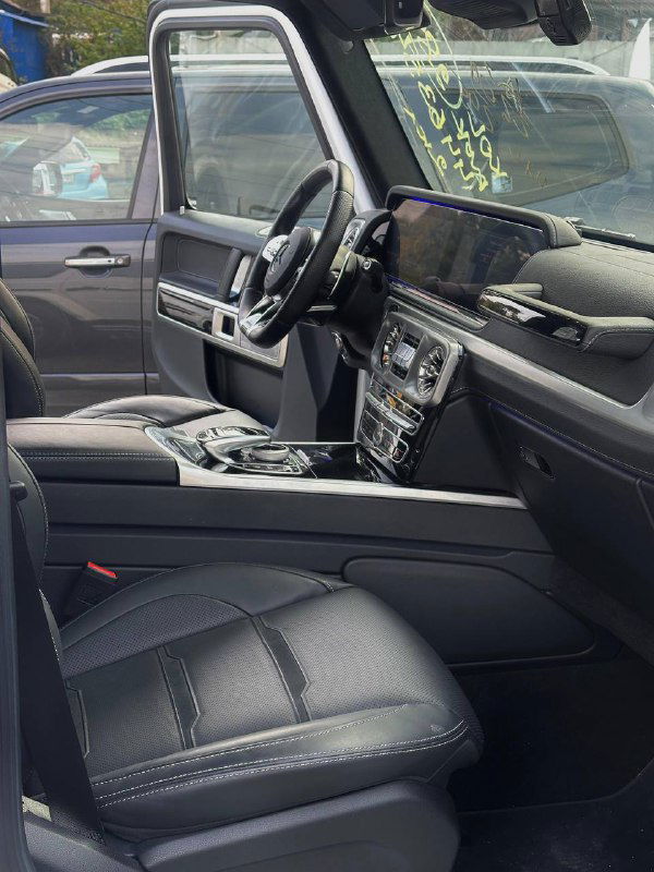 Вид салона Mercedes G63 AMG со стороны пассажира: передние кресла, панель и пространство между сиденьями, чёрная кожаная отделка.