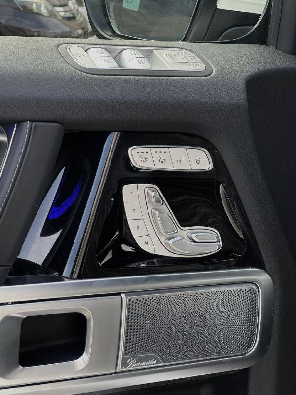Панель управления сиденьями и динамик Burmester в двери Mercedes G63 AMG, видны кнопки регулировки и декоративная отделка.