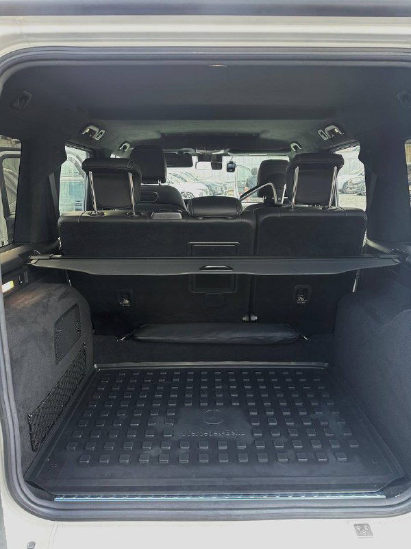 Багажное отделение Mercedes G63 AMG с открытой дверью: резиновый коврик, ровное грузовое пространство и вид на задние сиденья.