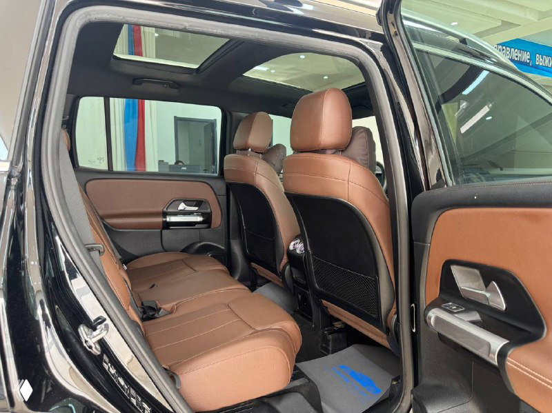 Задний ряд сидений Mercedes GLB с коричневой кожей: видно пространство для ног, подголовники и обшивку дверей в салоне дилера.