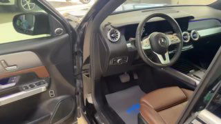 Косой вид на водительскую дверь и панель управления сиденьем Mercedes GLB: видно коврик, педали и часть салона со стороны водителя.