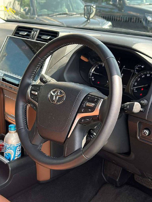 Рулевое колесо и приборная панель Toyota Prado — крупный план рулевого колеса с логотипом Toyota и мультимедийным дисплеем на торпедо.