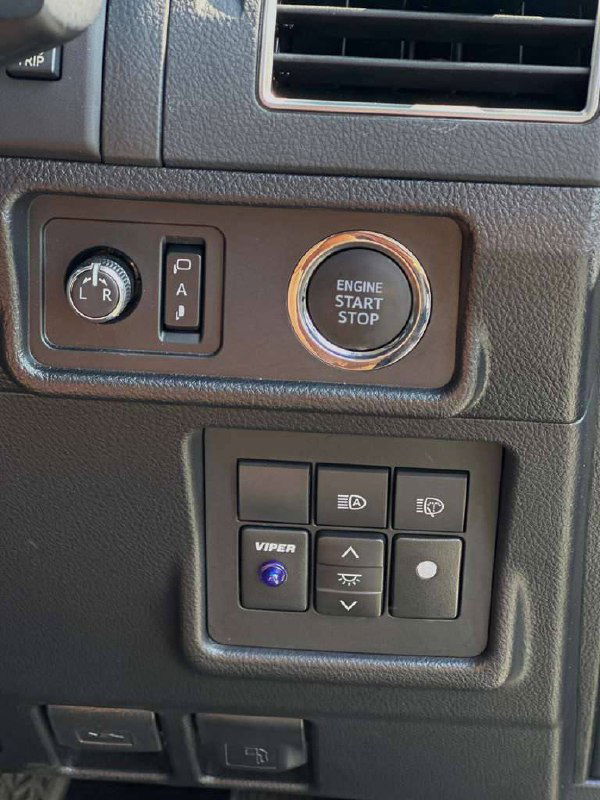 Кнопка запуска двигателя (ENGINE START STOP) и блок переключателей рядом с рулевой колонкой на панели управления Toyota Prado — вид крупным планом.