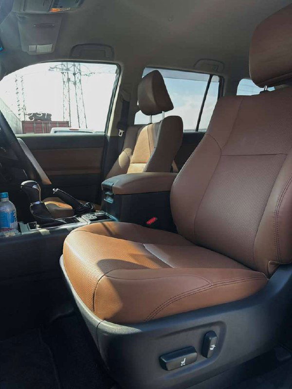 Вид на передние сиденья и центральную консоль Toyota Prado под углом — коричневый салон, состояние обивки и пространство для пассажиров.