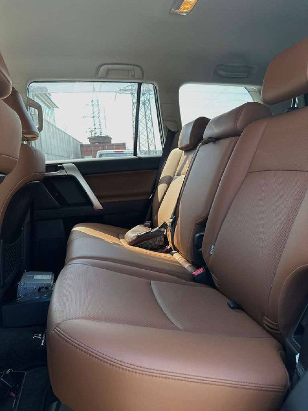 Второй ряд сидений Toyota Prado в коричневой обивке — три посадочных места, ремни безопасности и простор для пассажиров на заднем ряду.