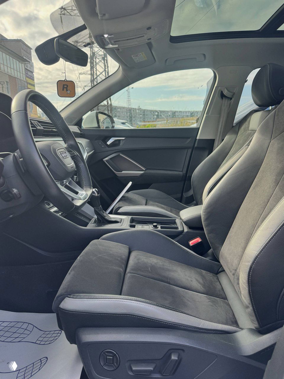 Фрагмент центральной панели и зоны селектора с органами управления, кнопками помощи при парковке и отделкой вокруг рычага передач.