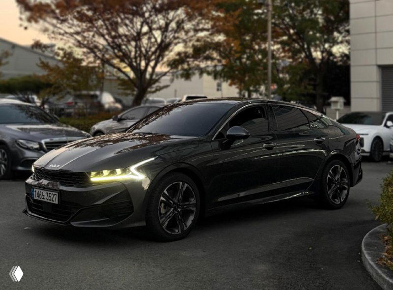 Боковой ракурс чёрного KIA K5, автомобиль в профиль на стоянке, видны лёгкие отражения в боковых панелях и стильные легкосплавные диски, подчёркнута форма кузова.