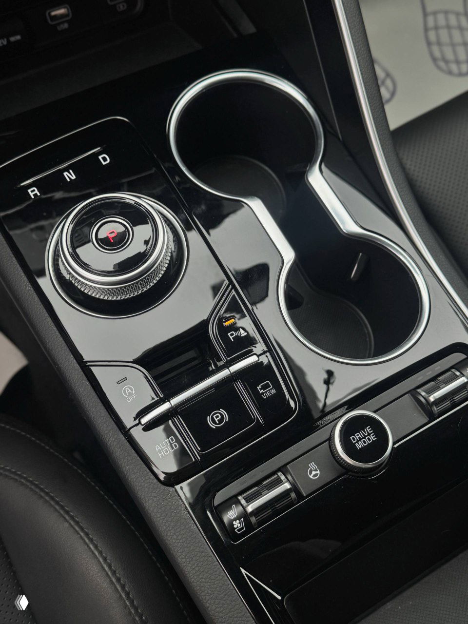 Детализация центральной консоли: шайба селектора передач, кнопки паркинга, два подстаканника и элементы управления режимами движения.