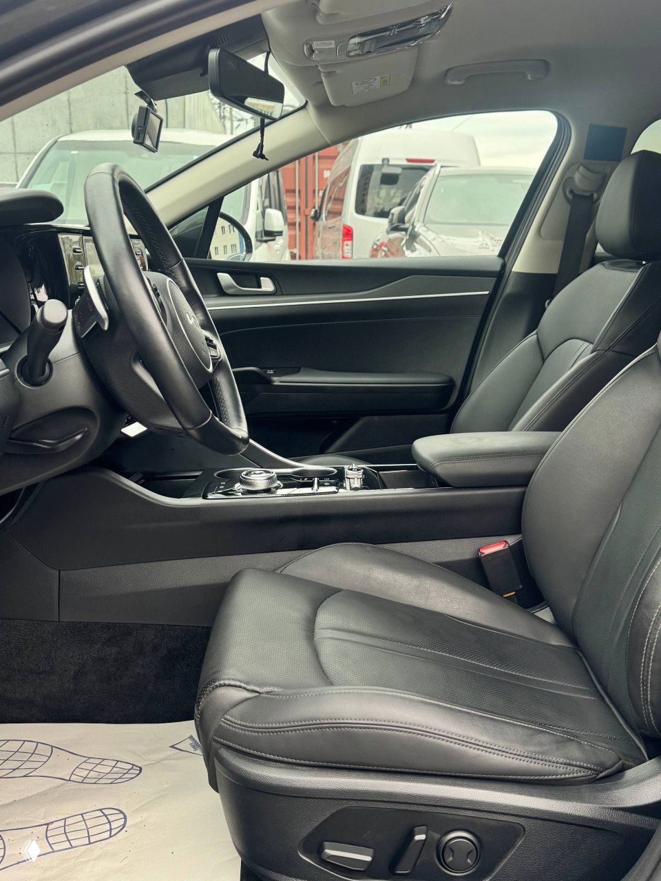 Переднее кресло водителя KIA K5 с кожаной обивкой, вид сбоку на посадочное место, регулировки и центральная консоль на заднем фоне.