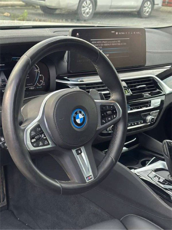 Салон BMW 530e: крупный план рулевого колеса с логотипом BMW и элементами управления в оформлении M‑Sport, панель приборов видна частично.