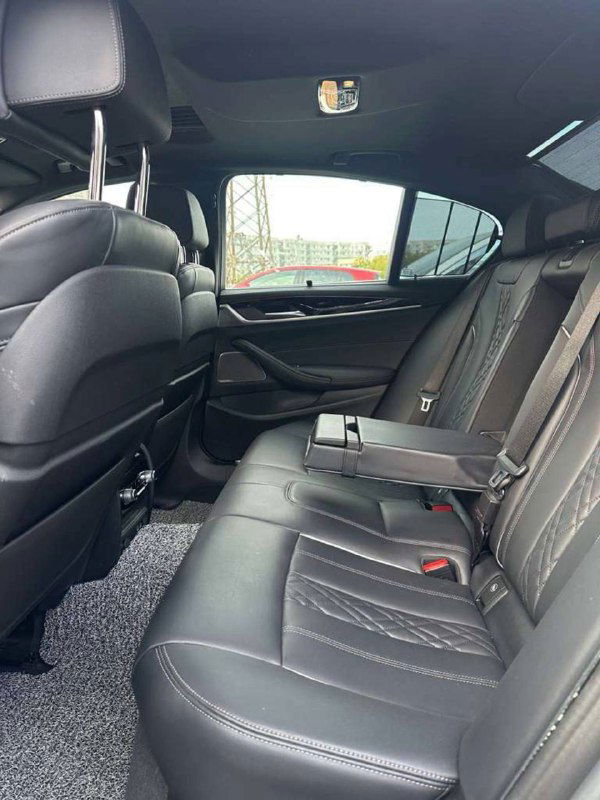 Вид на задние сиденья BMW 5‑Series: складной подлокотник, кожаная обивка и простор для пассажиров в заднем ряду — общий план салона.