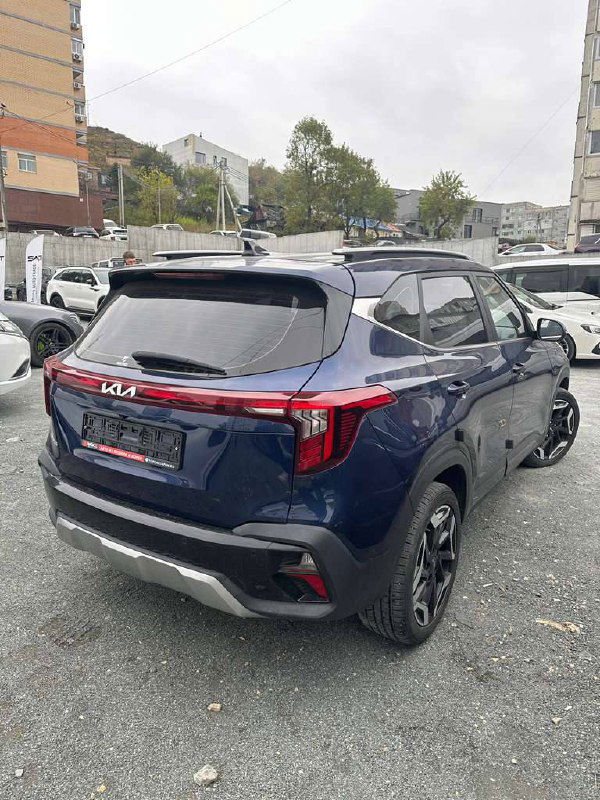 Общий вид сзади KIA Seltos тёмно‑синего цвета: задняя оптика, багажная дверь и серебристый диффузор на парковке дилера.