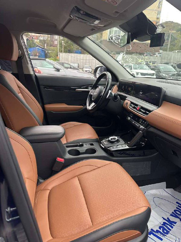 Широкий вид салона KIA Seltos с передними и частично задними сиденьями, панорамный вид кабины и отделка коричневой экокожей.