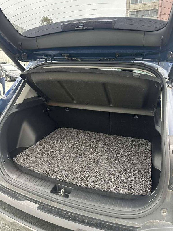 Багажное отделение KIA Seltos с поднятой крышкой, ровное пространство для вещей и коврик в багажнике на стоянке.