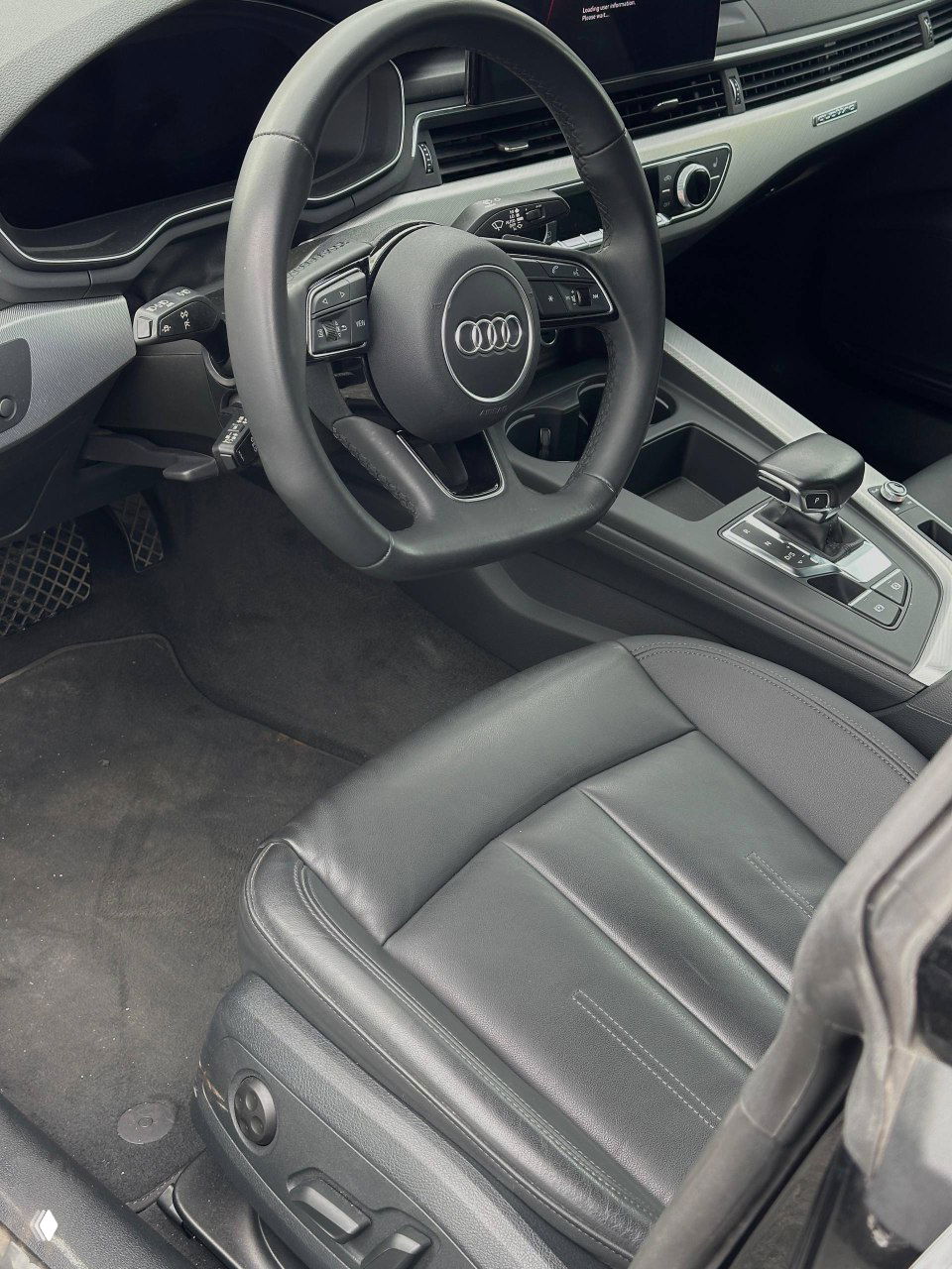 Руль Audi с логотипом бренда, панель приборов и часть переднего сиденья — обзор водительской зоны и элементов управления