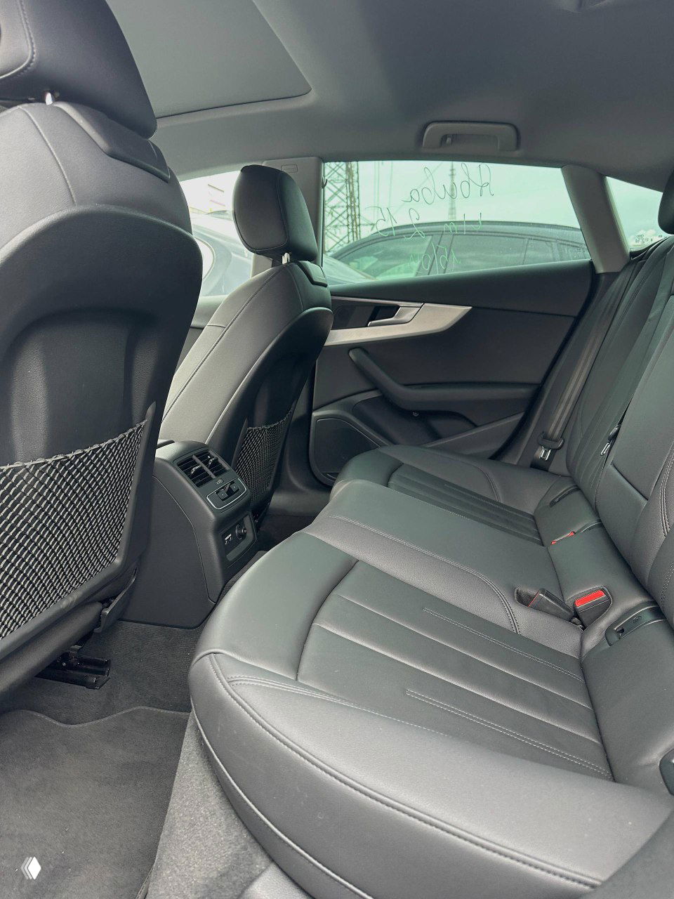 Задний ряд сидений Audi, чёрная обивка и пространство для ног; камера показывает состояние заднего салона и отделку дверей