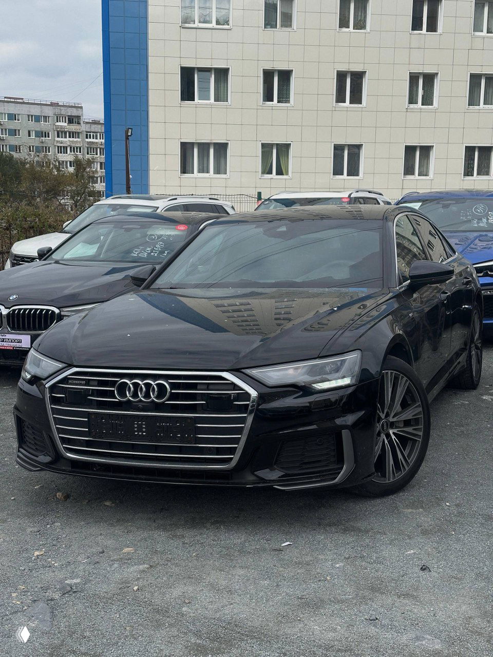 Чёрный Audi A6 45TFSI, общий вид спереди; автомобиль на городской стоянке, видна радиаторная решётка и передний бампер