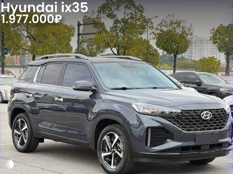Фото серого Hyundai ix35 2021 года на открытой парковке; изображение показывает боковой и фронтальный ракурс автомобиля и городской пейзаж на заднем плане.