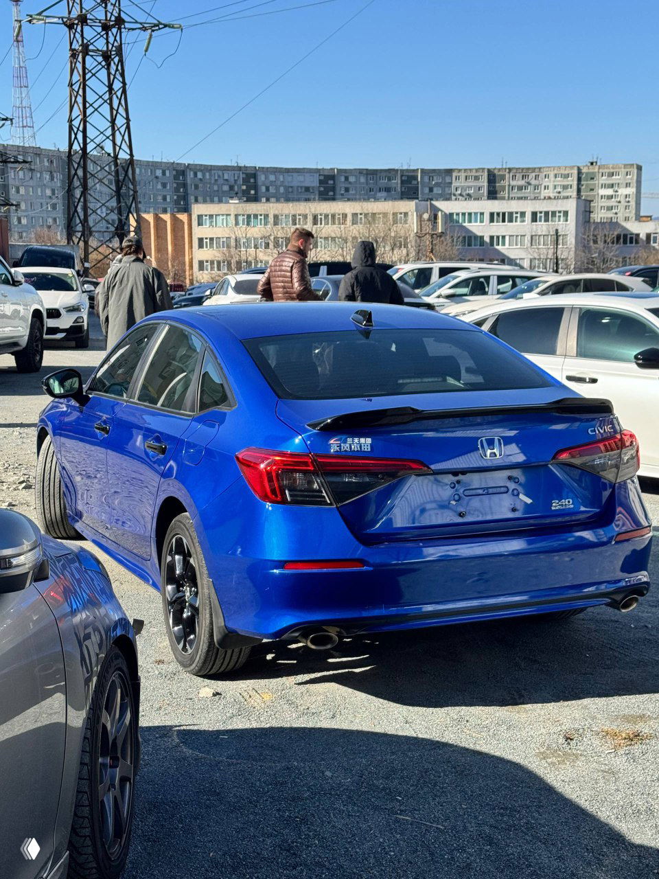 Задний ракурс синего Honda Civic 2021 на стоянке, видно багажник, шильдик Civic и окружение торговой площадки автопарка.