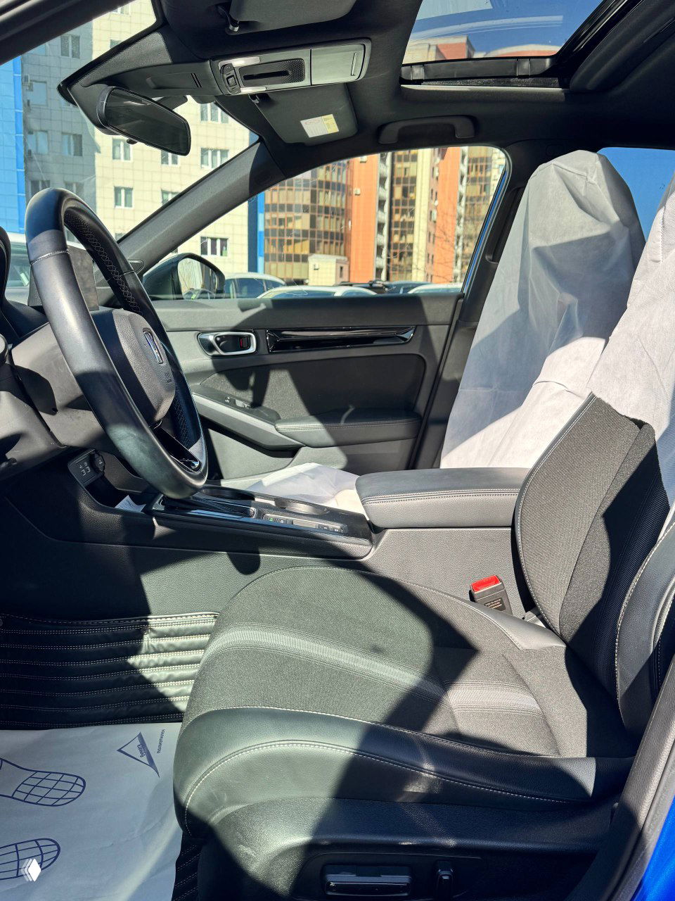 Вид на переднее пассажирское сиденье и панораму салона Honda Civic 2021: состояние обивки, подлокотник и часть панорамной крыши видно на фото.