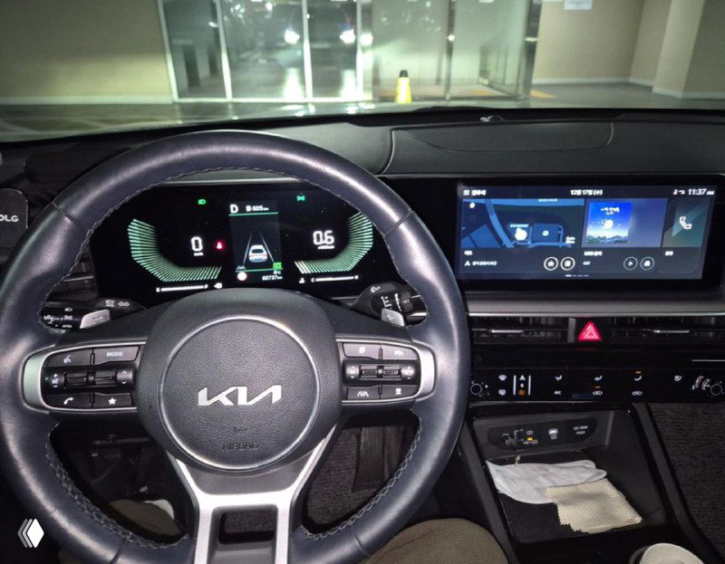 Крупный план салона KIA K5: рулевое колесо с логотипом KIA, цифровая приборная панель и мультимедиа экран на торпедо видны чётко.