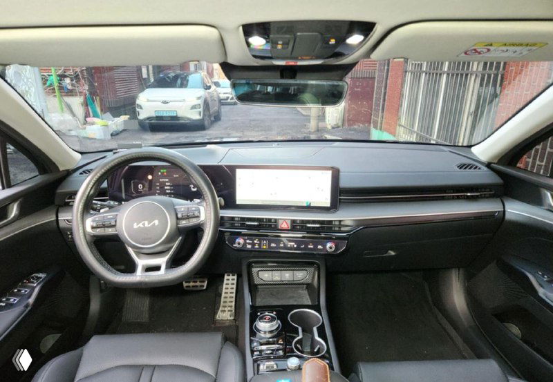 Широкий вид салона KIA K5 с пассажирского места: торпедо, большой экран мультимедиа, центральная консоль и подстаканники на панели видны.