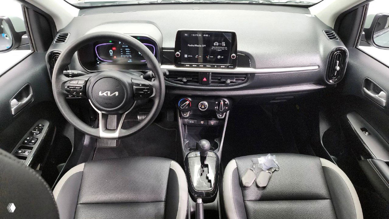 Передняя панель салона KIA Morning 2025: руль с логотипом KIA, приборная панель, центральная консоль и сиденья с двухцветной обивкой.