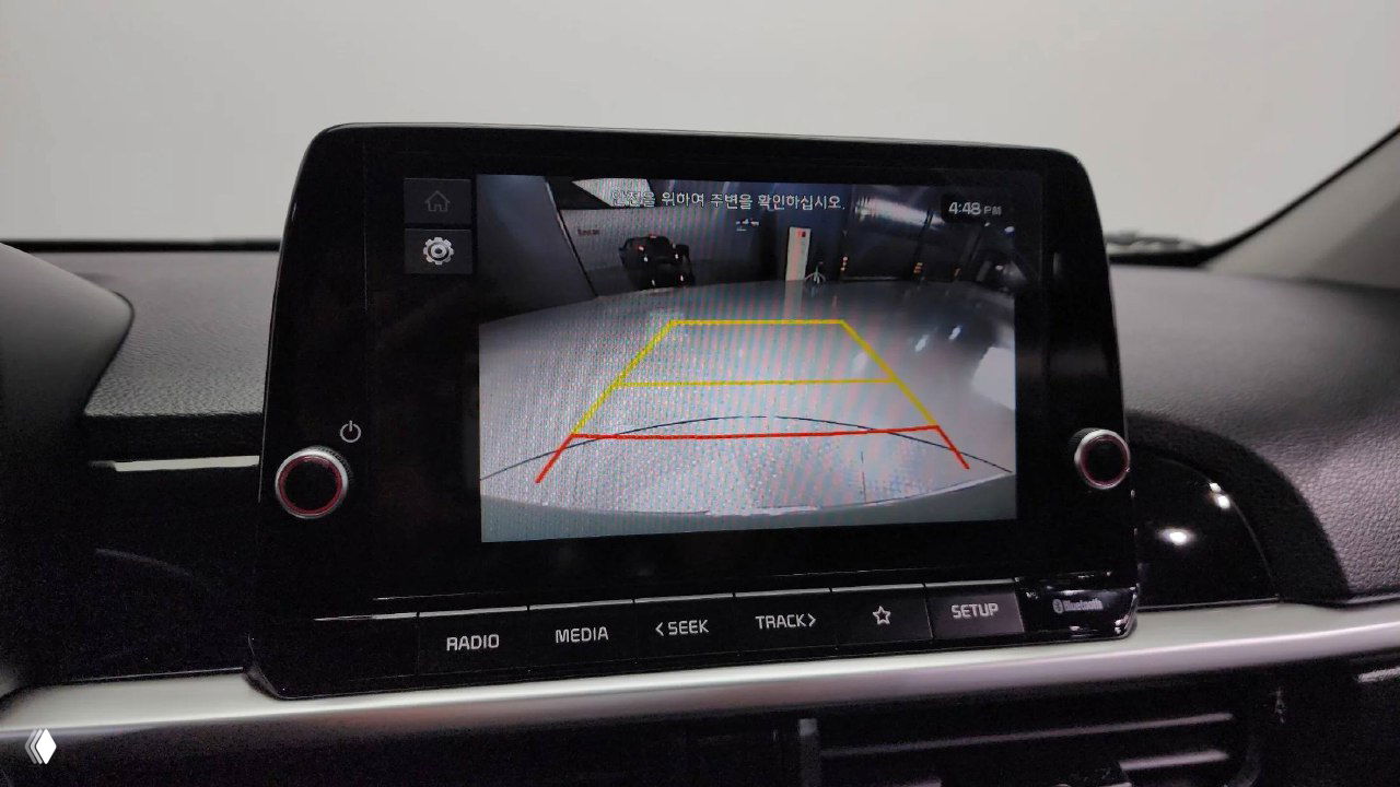 Экран мультимедиа KIA Morning 2025 показывает изображение с камеры заднего вида с разметкой парковки, вид крупным планом внутри салона.