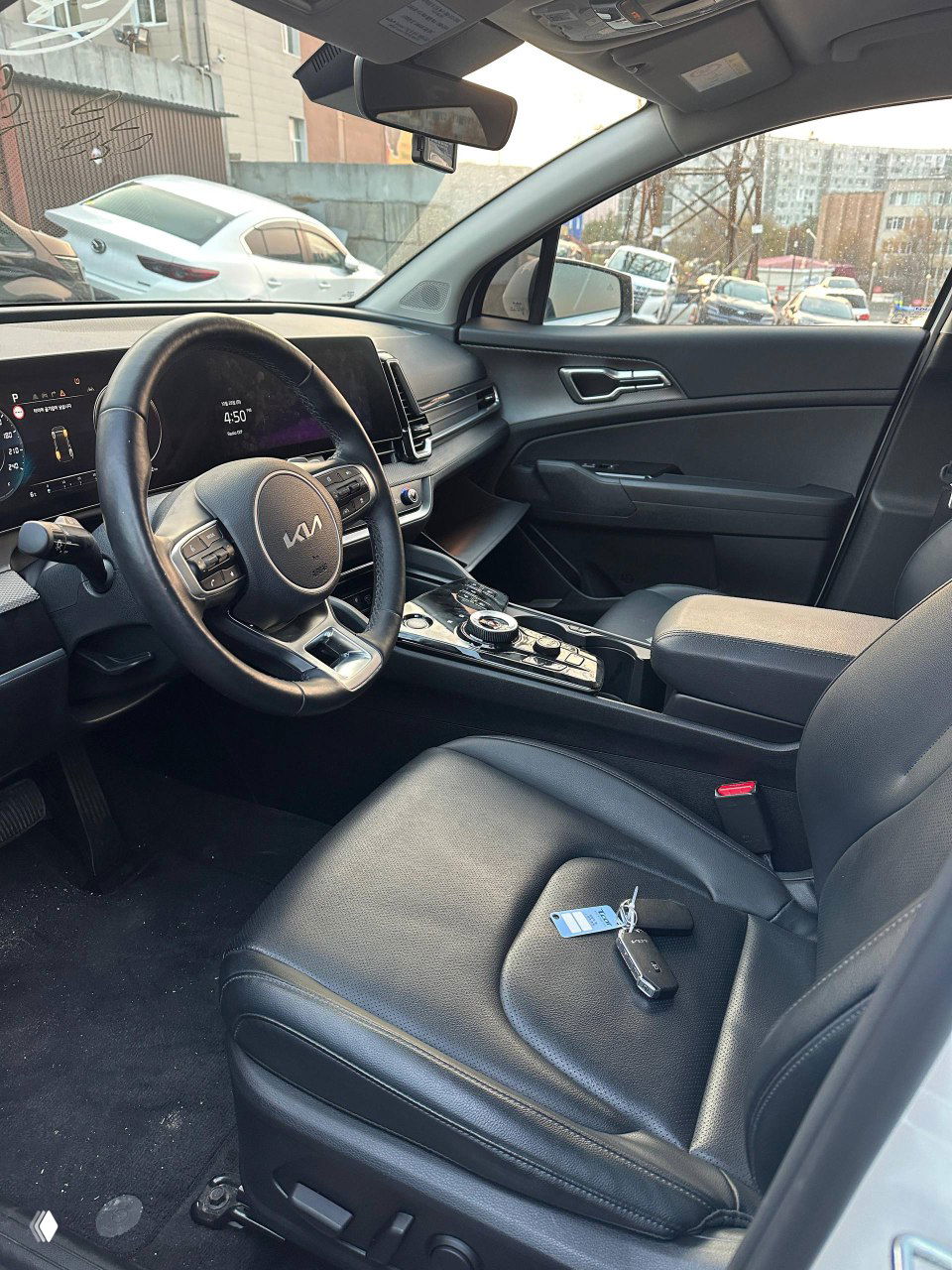 Салон KIA Sportage, вид переднего ряда и центральной консоли с селектором и электронными элементами, видны кожаные сиденья и ключ на сиденье.