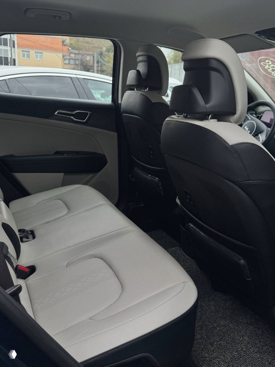 Передние сиденья KIA Sportage светлой обивки, вид на водительское место, подлокотник и часть центральной консоли — чистая и неистёкшая обивка.