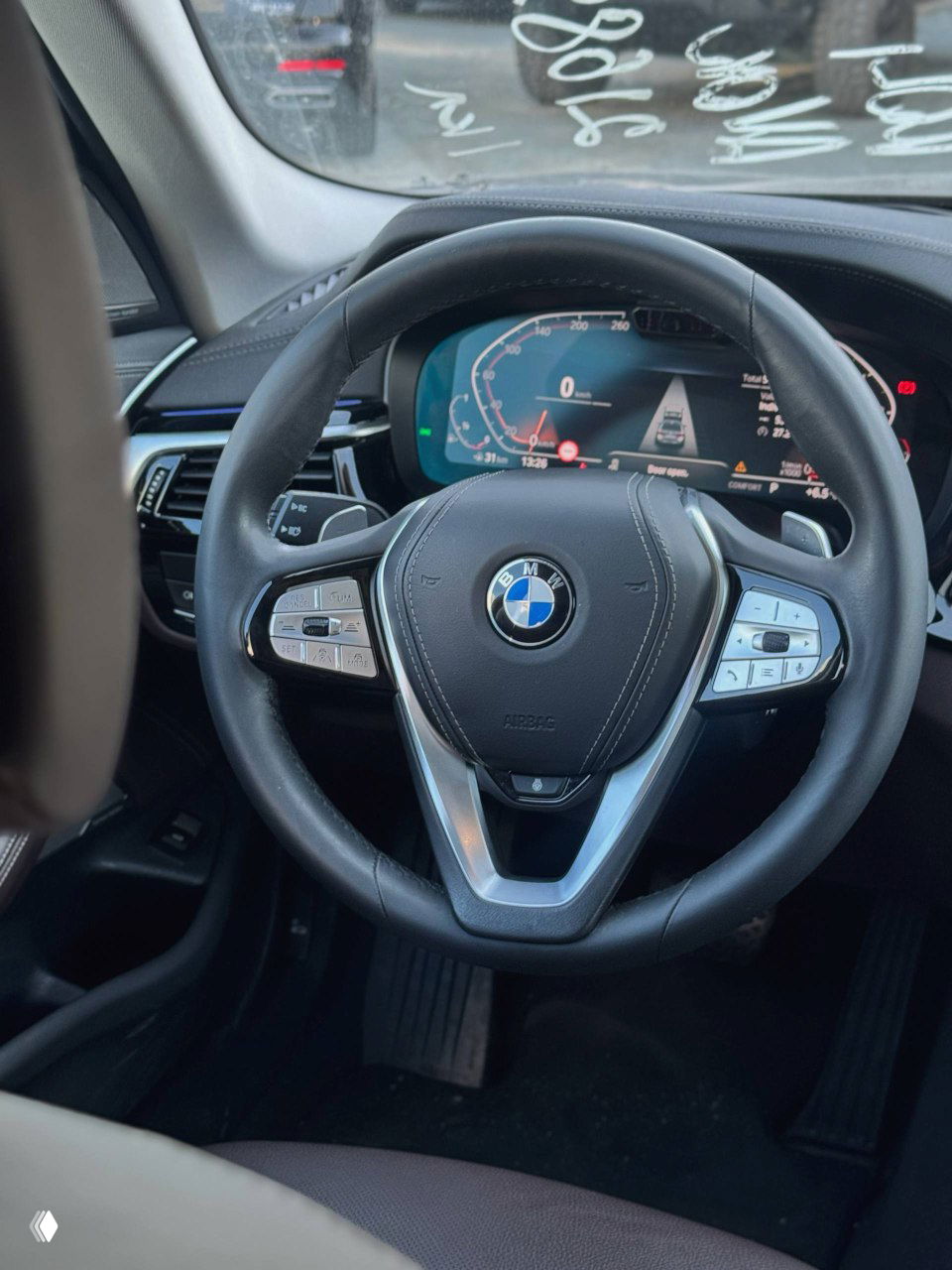 Руль BMW с крупным планом: мультируль с кнопками управления, логотип BMW в центре и вид на цифровую комбинацию приборов позади руля.