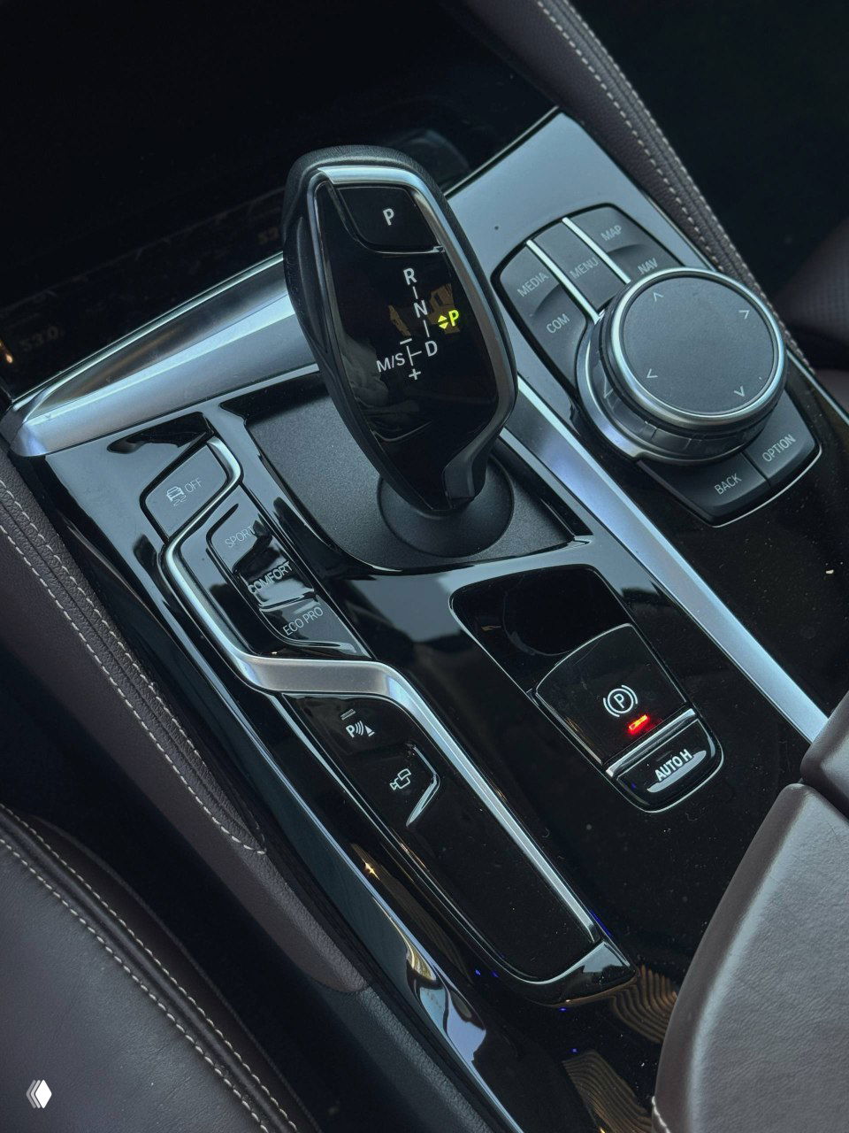 Селектор передач BMW вблизи: современный рычаг АКПП, переключатели режимов движения и поворотный контроллер мультимедиа на центральном тоннеле.