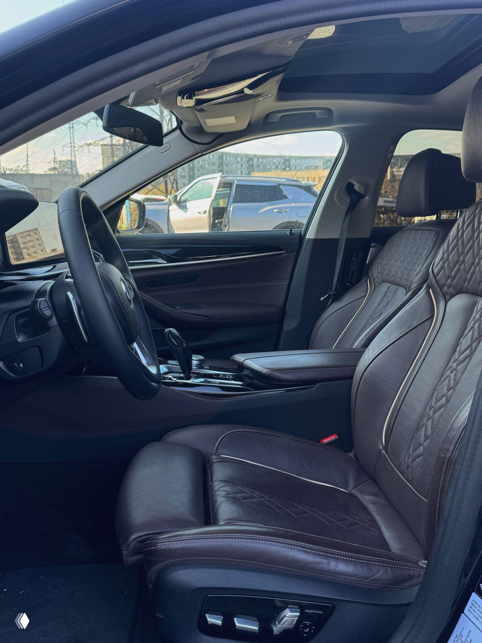 Вид на переднее пассажирское сиденье и центральный подлокотник BMW 530i: коричневая кожаная обивка, электрорегулировки и панорамная крыша частично видна.