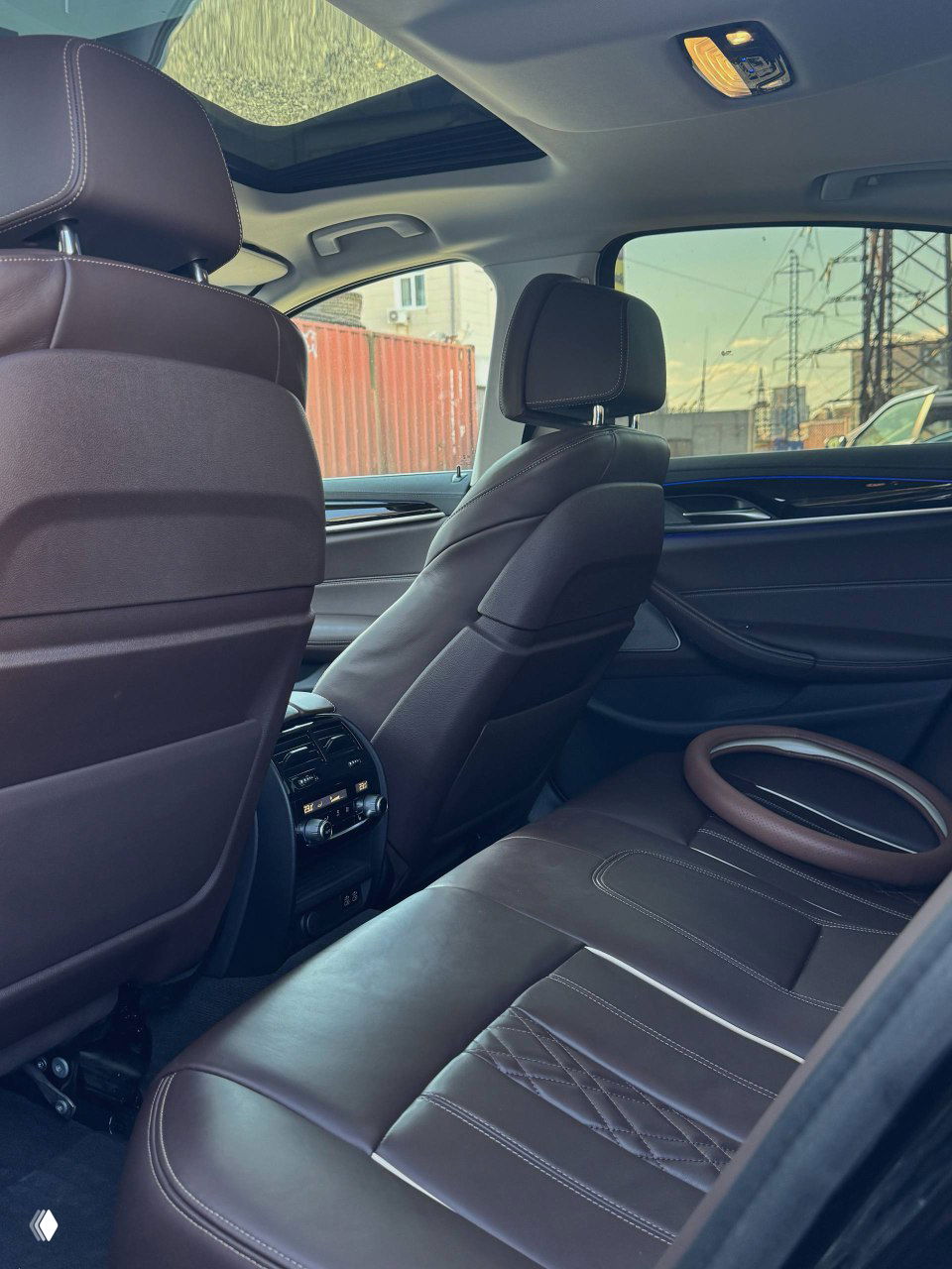 Вид на задний ряд сидений BMW 530i: тёмная коричневая кожа, центральный подлокотник и климат-контроль для задних пассажиров, общий план салона.