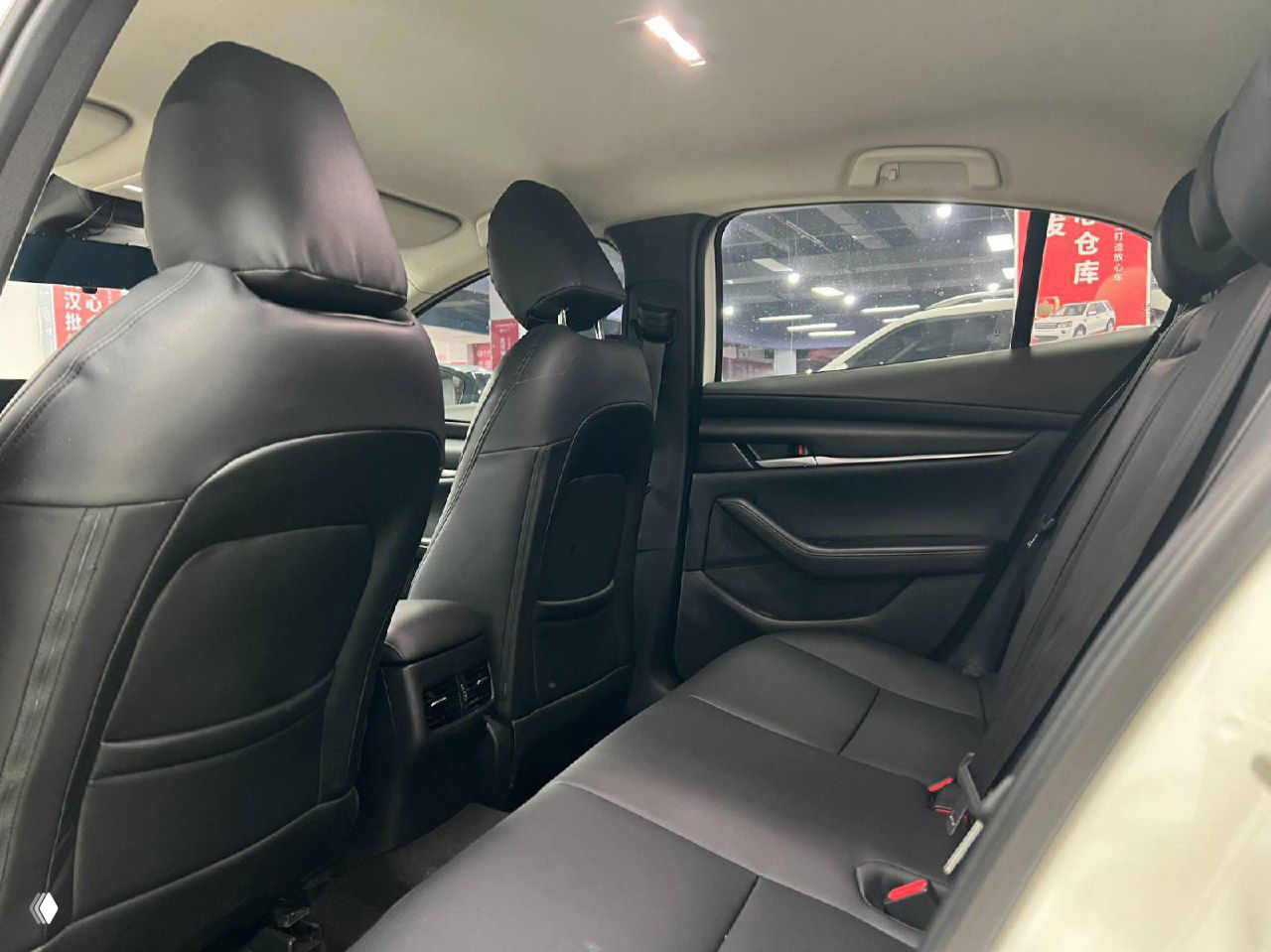 Переднее пассажирское сиденье и центральная часть салона Mazda 3 Axela: чёрная обивка, швы на сиденье и элементы дверной обшивки в интерьере автомобиля в Китае.