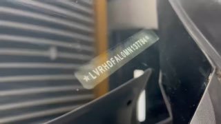 Крупный план VIN-пластинки Mazda 3 Axela за лобовым стеклом: разборчивые символы VIN и отражения потолочных светильников в шоуруме, видеокадр.