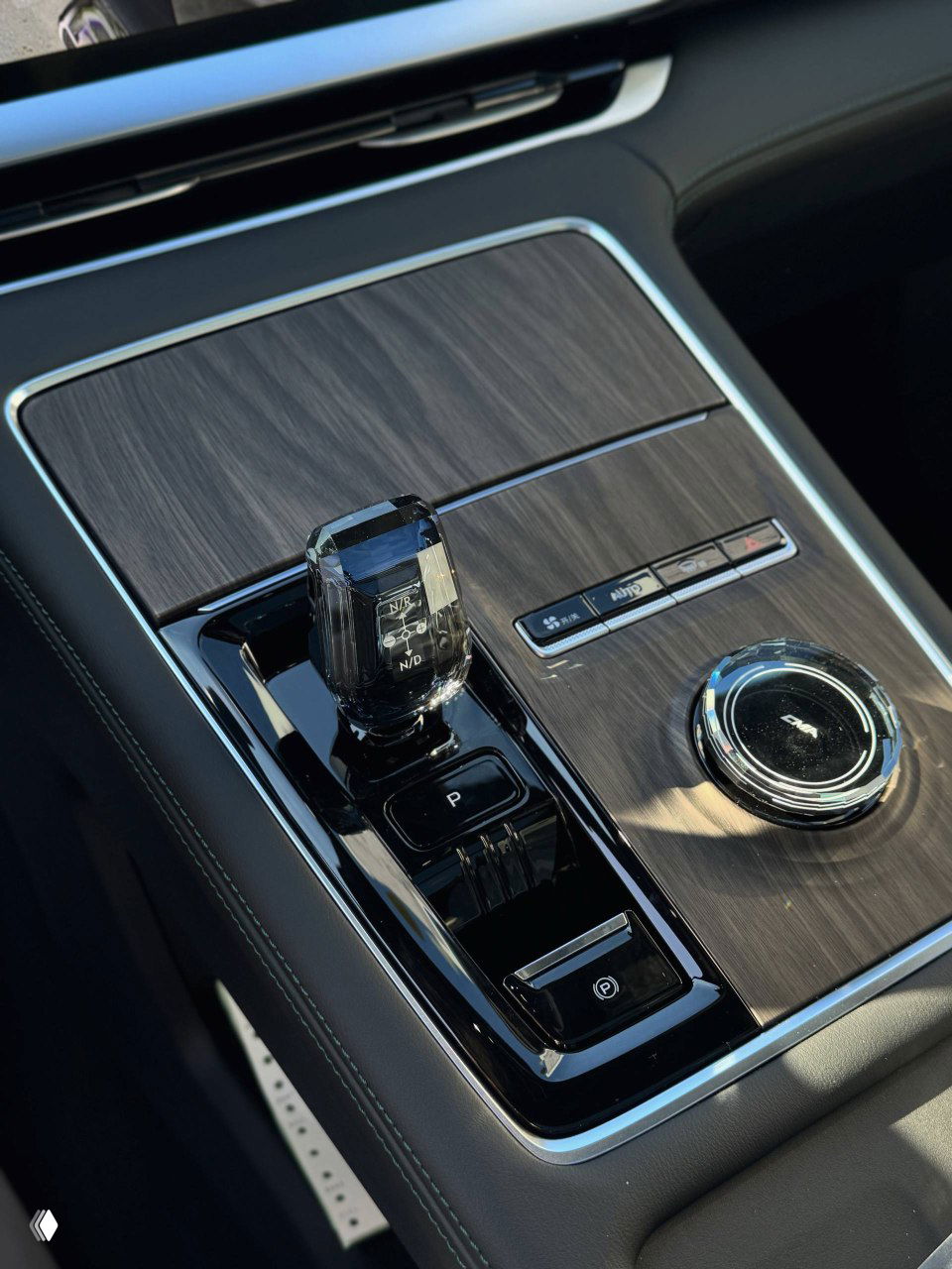 Селектор коробки передач Geely Monjaro на фоне деревянной вставки центральной консоли и вращающегося регулятора режимов, детальный снимок интерьера и отделки.