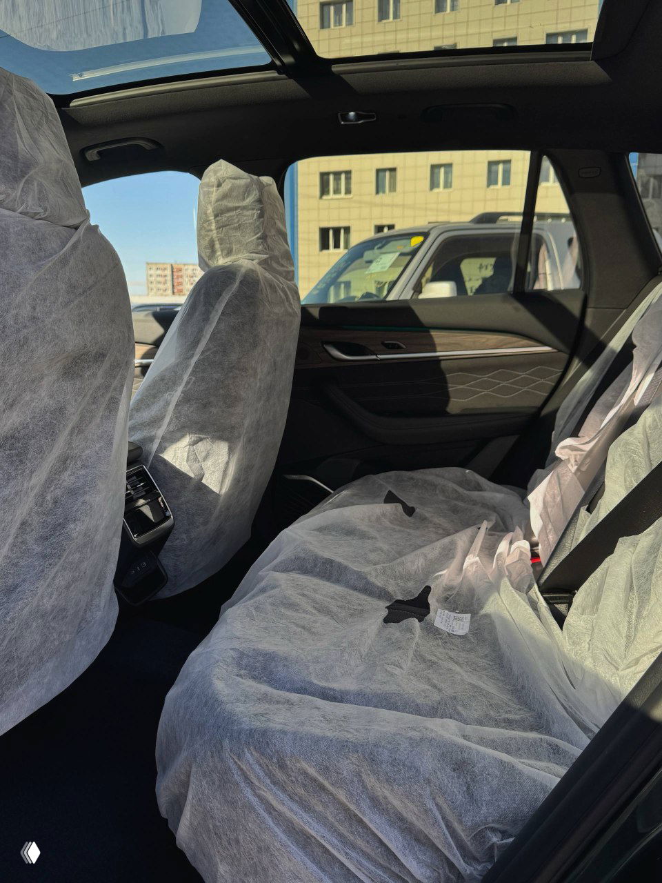 Задний ряд салона Geely Monjaro с защитными чехлами на сиденьях и панорамной крышей над ними, видна отделка дверей и пространство для пассажиров на фото.