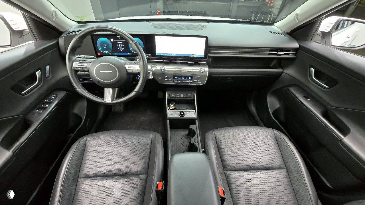 Общий вид салона Hyundai Kona: два широких дисплея, руль с многофункциональными кнопками, передние сиденья и центральный тоннель, чистое состояние.
