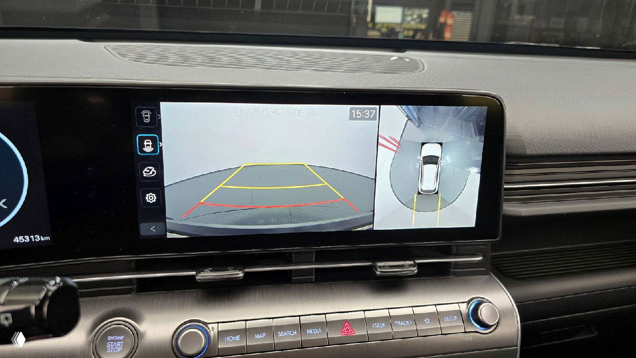 Крупный план центрального дисплея Hyundai Kona с изображением камеры заднего вида и кругового обзора, отображаются парковочные линии и окружение.