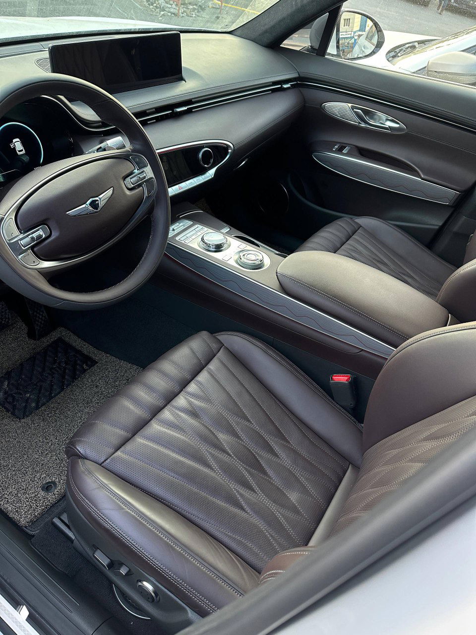 Интерьер Genesis GV70 — широкий вид на панель приборов, передние сиденья и мультимедийный экран; видна коричневая кожаная отделка и хромированные акценты в салоне.