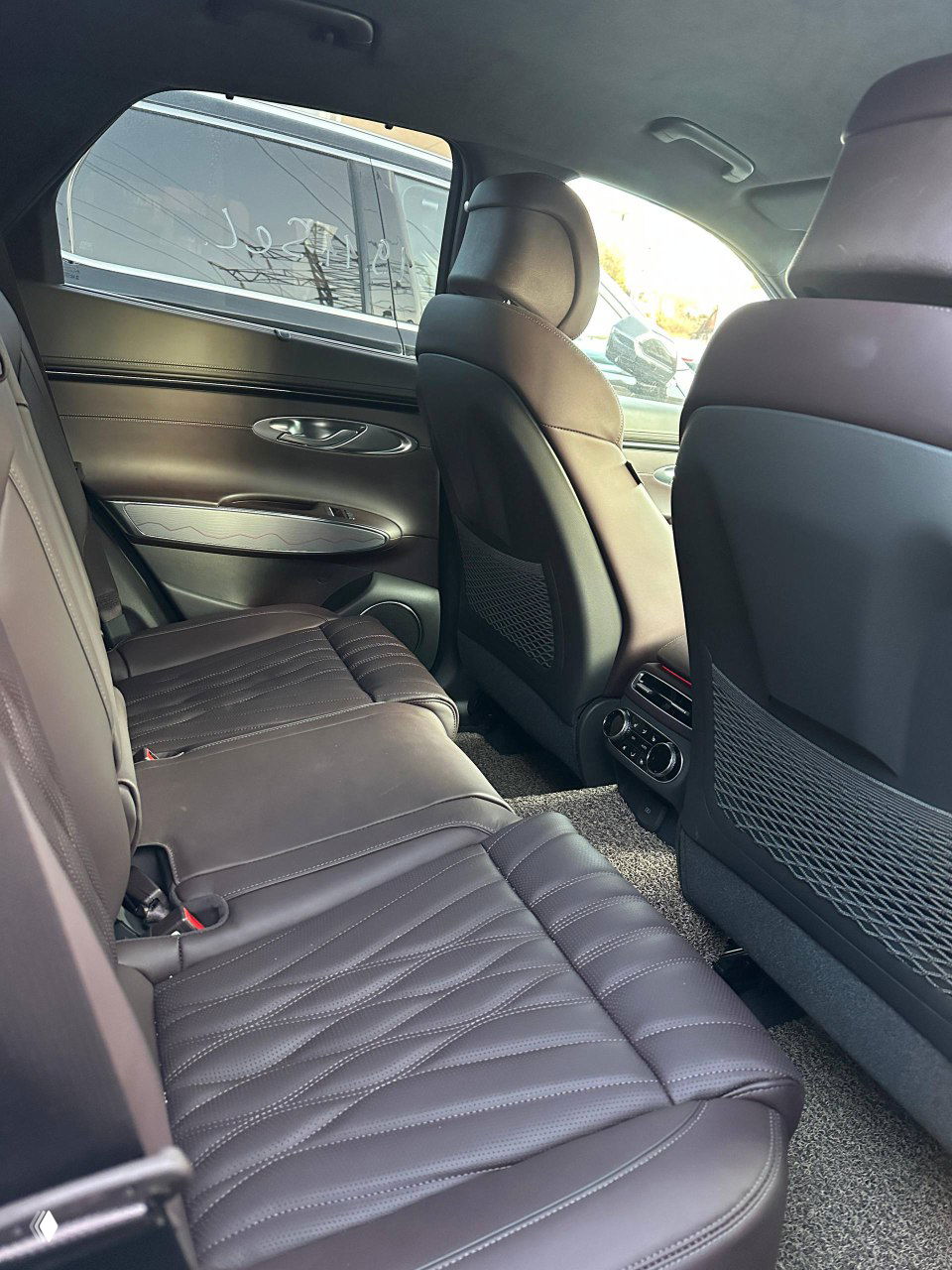 Задний ряд сидений Genesis GV70: коричневая перфорированная кожа, комфортная посадка, видны вентиляционные дефлекторы и задняя часть центральной консоли с регулировками.