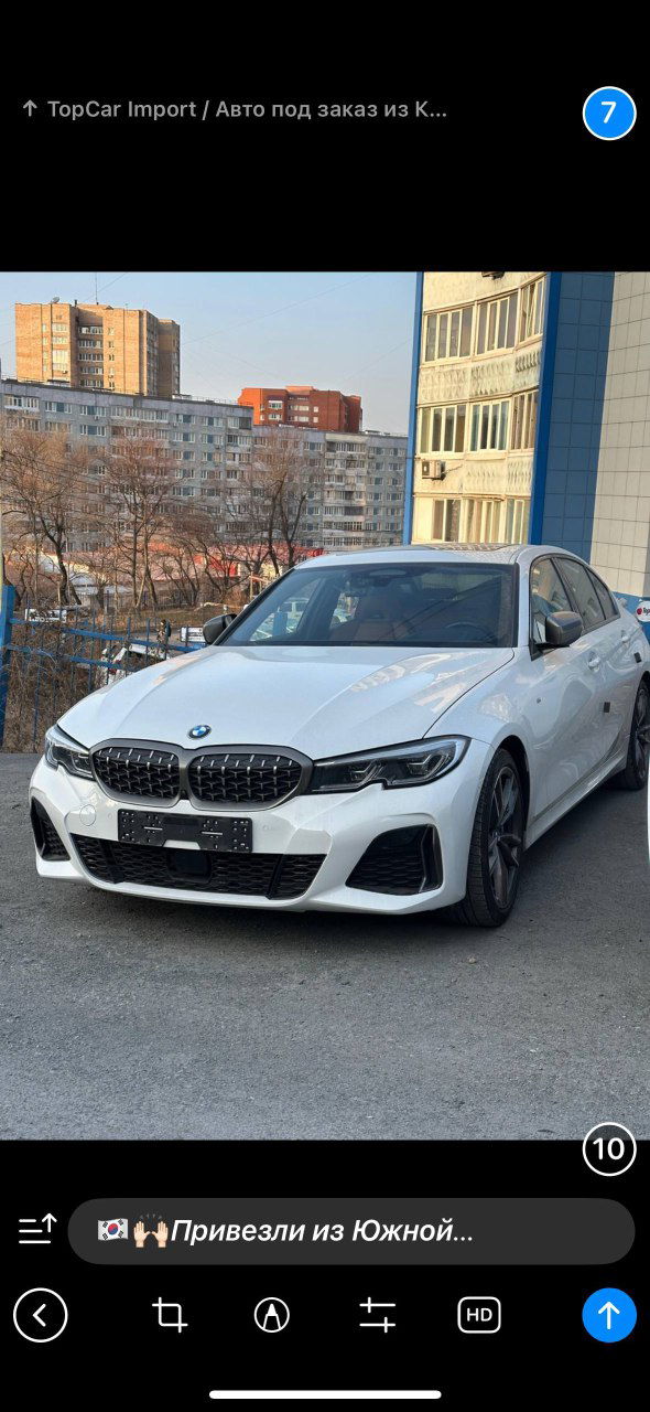 Фронтальный вид белого BMW 340i M‑Sport на фоне городской застройки; заметны характерные почки решётки, бампер M‑Sport и спортивные акценты экстерьера автомобиля.